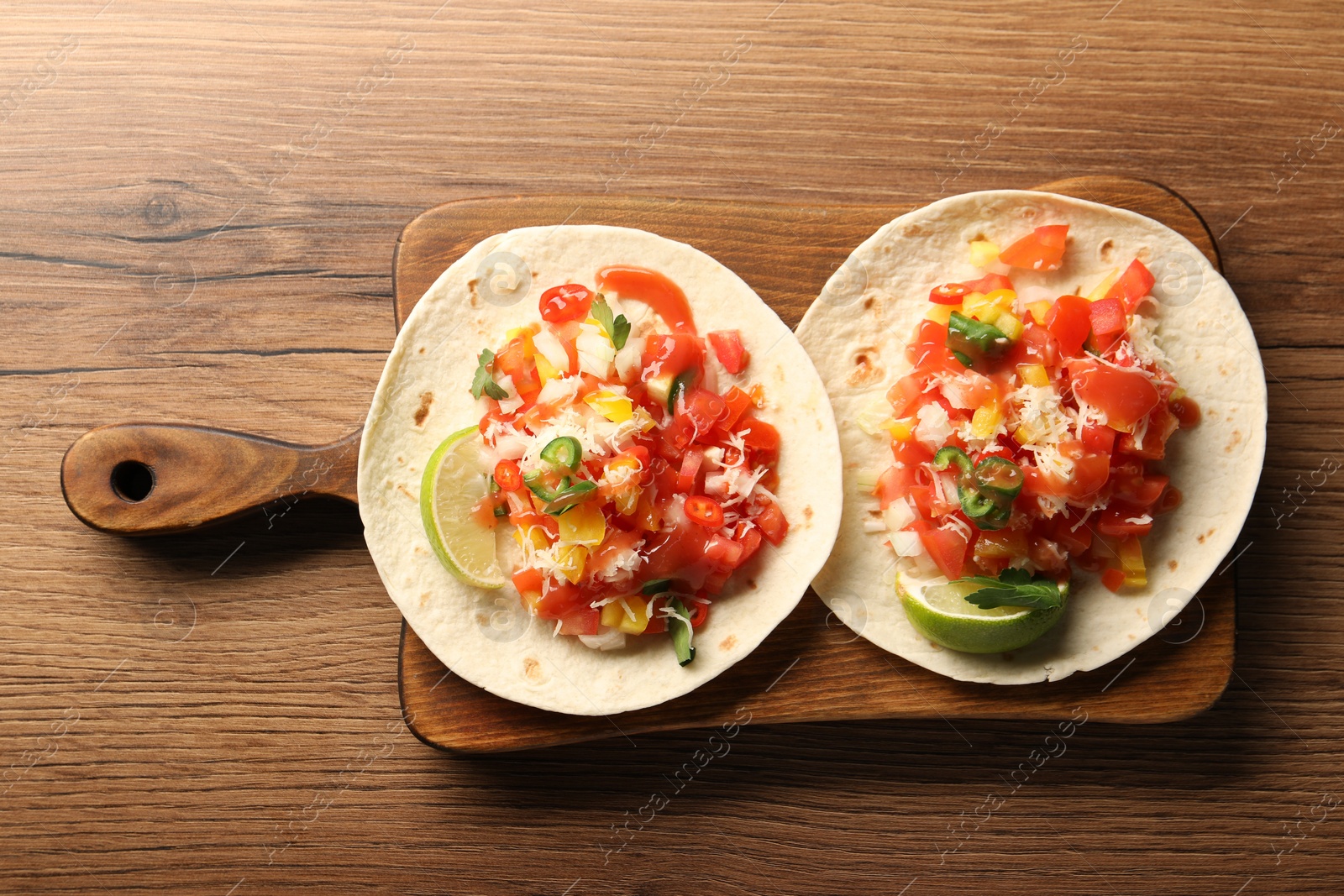 Photo of Delicious tacos with vegetables, green onion, lime and ketchup on wooden table, top view