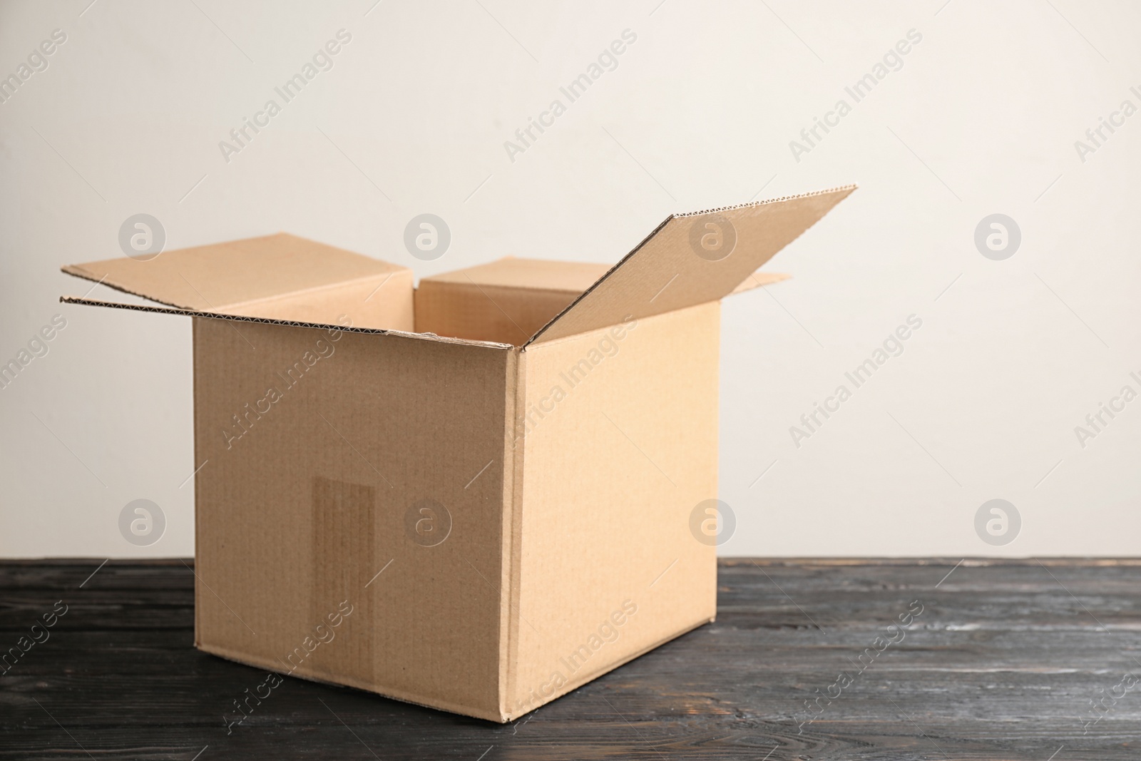 Photo of Open cardboard box on black wooden table against beige background