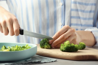 Photo of Woman cutting boiled broccoli at table, closeup. Child's food