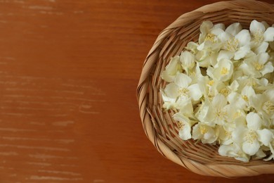 Photo of Beautiful white jasmine flowers in wicker basket on wooden table, top view. Space for text