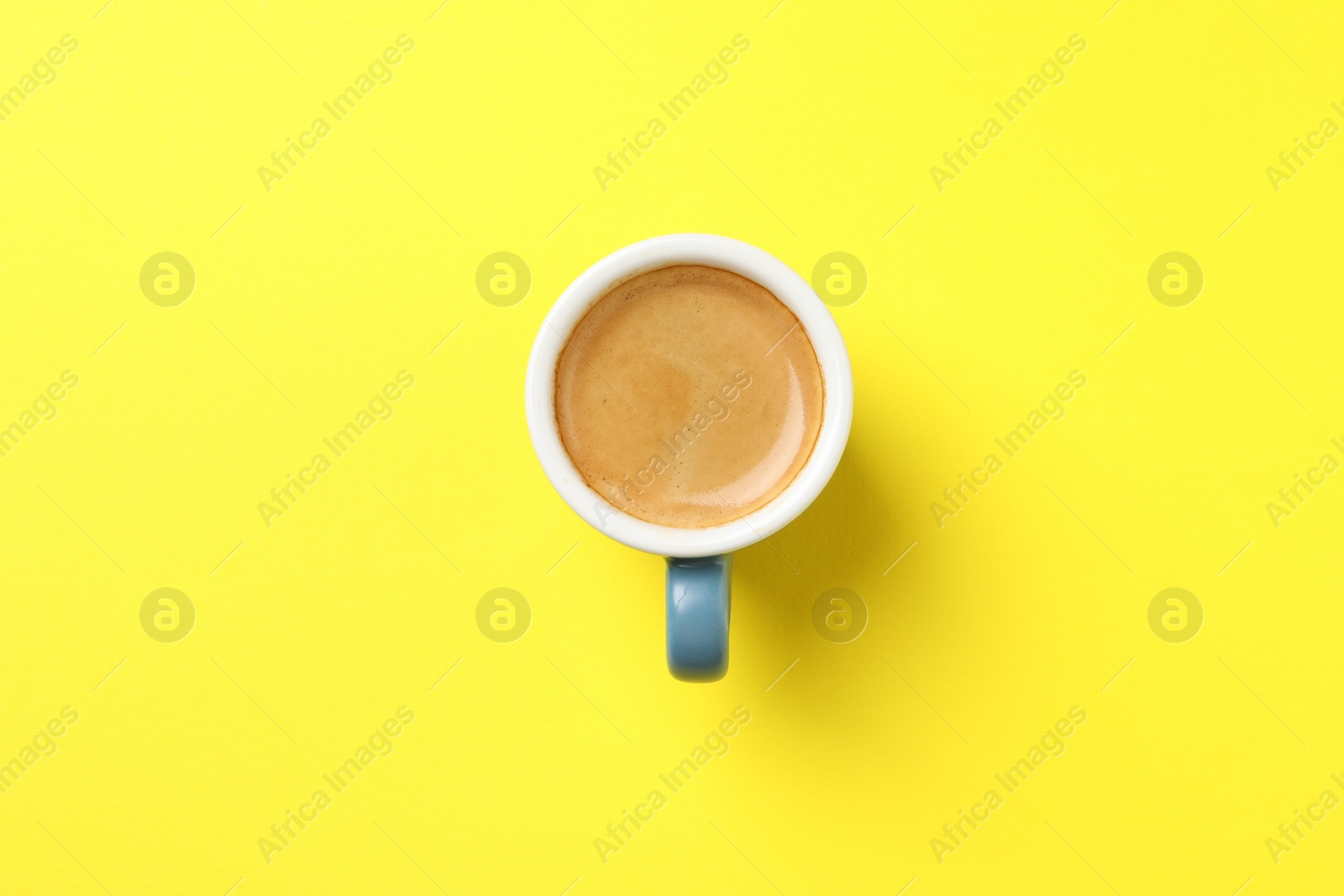 Photo of Aromatic coffee in cup on yellow background, top view