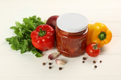 Photo of Glass jar of delicious canned lecho and fresh ingredients on white wooden table