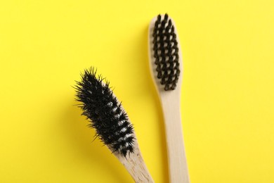 Two bamboo toothbrushes on yellow background, flat lay