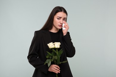 Photo of Sad woman with white rose flowers mourning on light grey background. Funeral ceremony