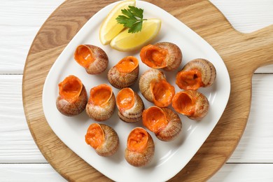 Delicious cooked snails with lemon and parsley on white wooden table, top view