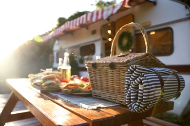 Photo of Wicker basket with picnic blanket on wooden table near trailer. Camping season