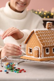 Photo of Woman decorating gingerbread house with icing at table, closeup