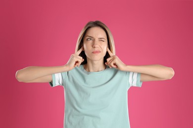 Photo of Emotional young woman covering her ears with fingers on pink background