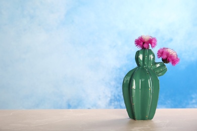 Photo of Trendy cactus shaped ceramic vase with flowers on table