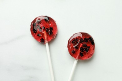 Sweet colorful lollipops with berries on white marble table, flat lay