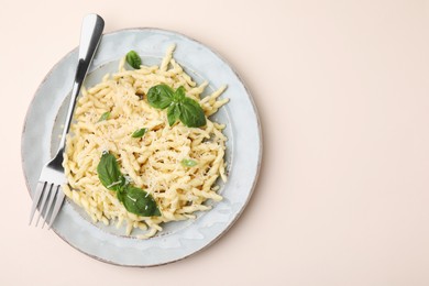 Photo of Plate of delicious trofie pasta with cheese, basil leaves and fork on beige background, top view. Space for text