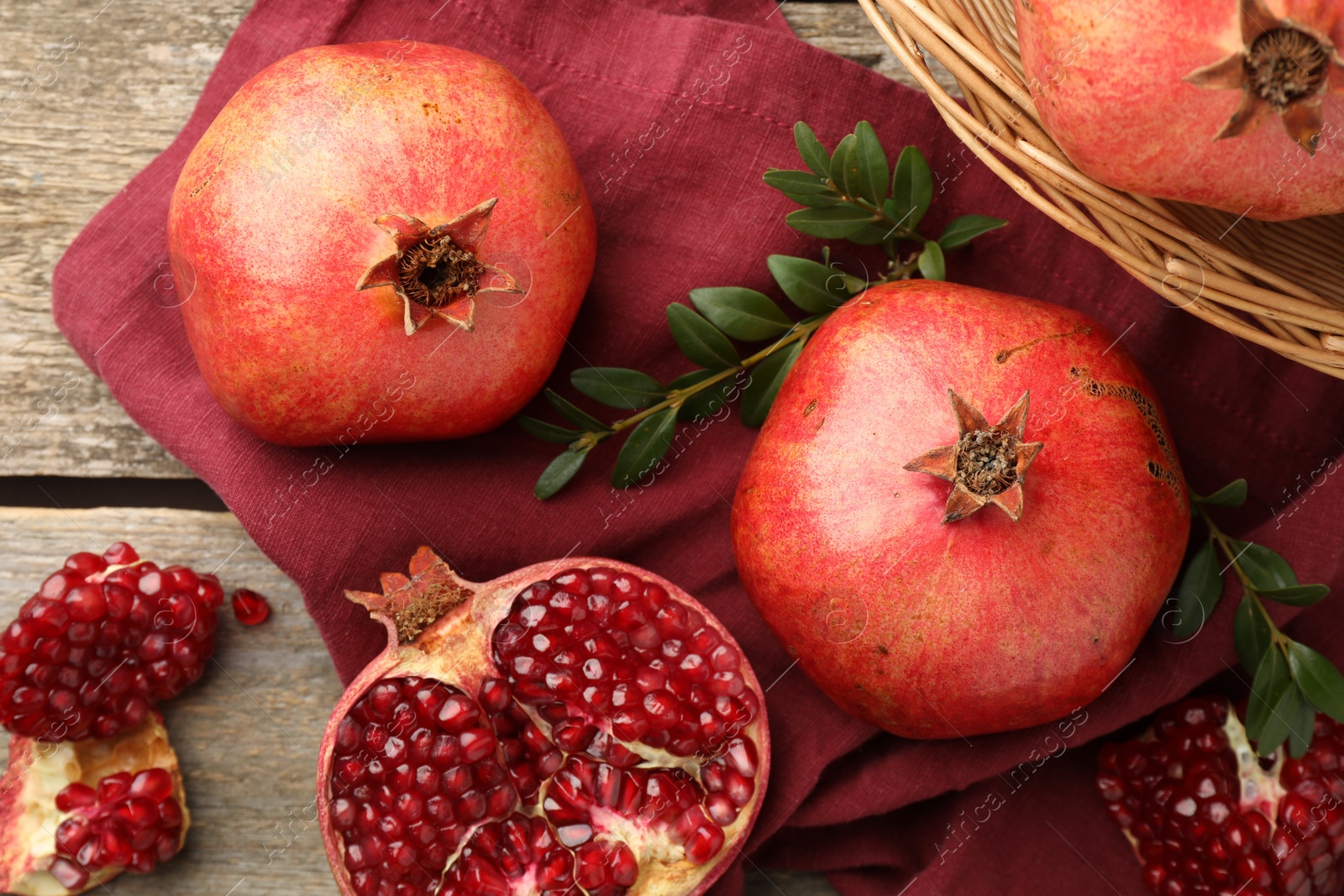 Photo of Fresh pomegranates and green leaves on wooden table, top view