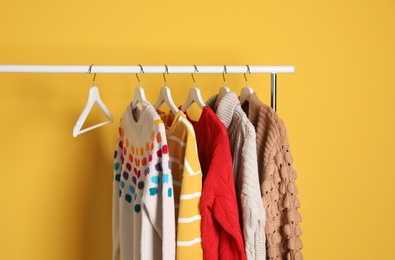 Collection of warm sweaters hanging on rack against color background