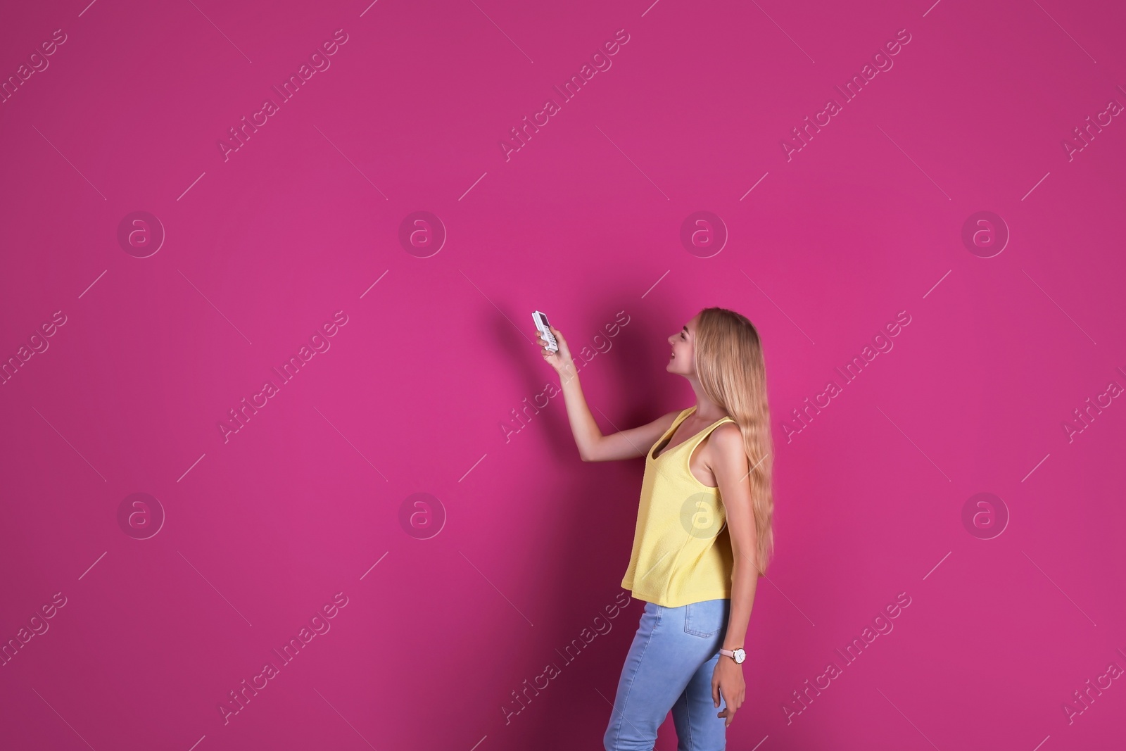 Photo of Young woman operating air conditioner with remote control on color background