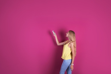 Photo of Young woman operating air conditioner with remote control on color background