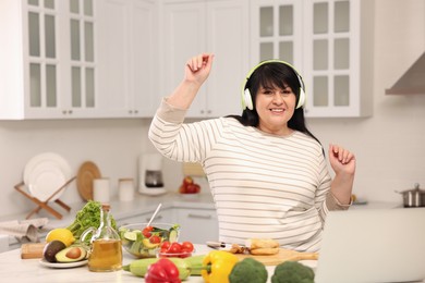 Happy overweight woman with headphones dancing while cooking in kitchen