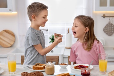 Photo of Little children having fun during breakfast at table in kitchen