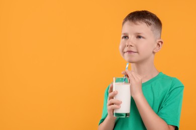 Photo of Cute boy with glass of fresh milk on orange background, space for text