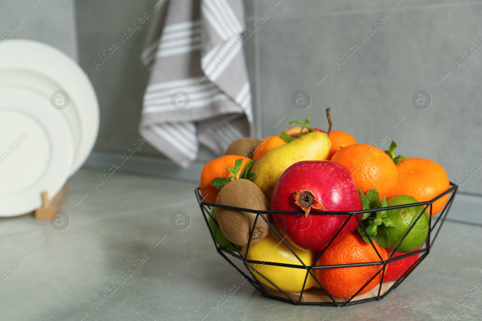 Photo of Metal basket with different ripe fruits on grey countertop. Space for text