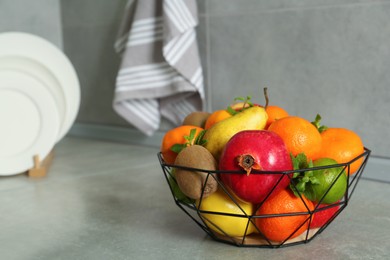 Metal basket with different ripe fruits on grey countertop. Space for text
