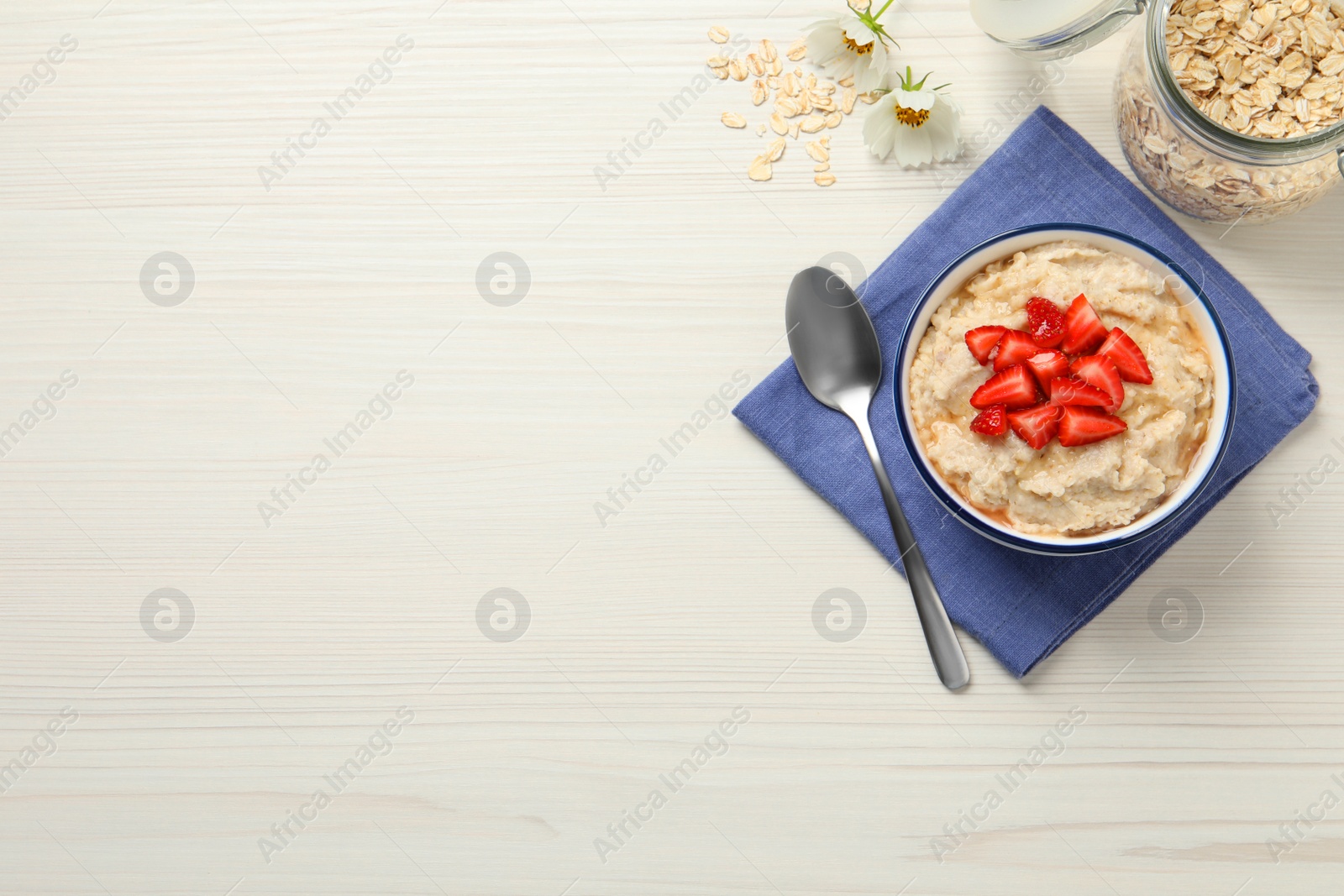 Photo of Tasty oatmeal porridge with strawberries served on white wooden table, flat lay. Space for text