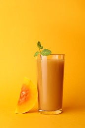 Tasty pumpkin juice in glass and cut pumpkin on orange background