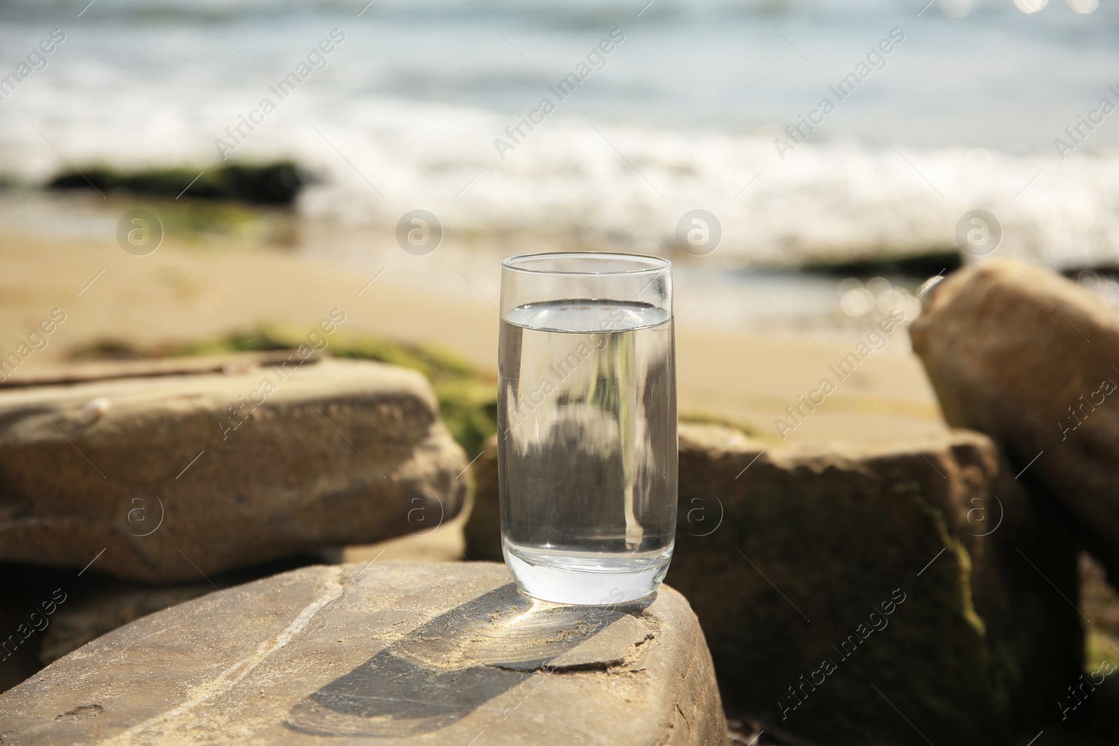 Photo of Glass of fresh water on stone near sea