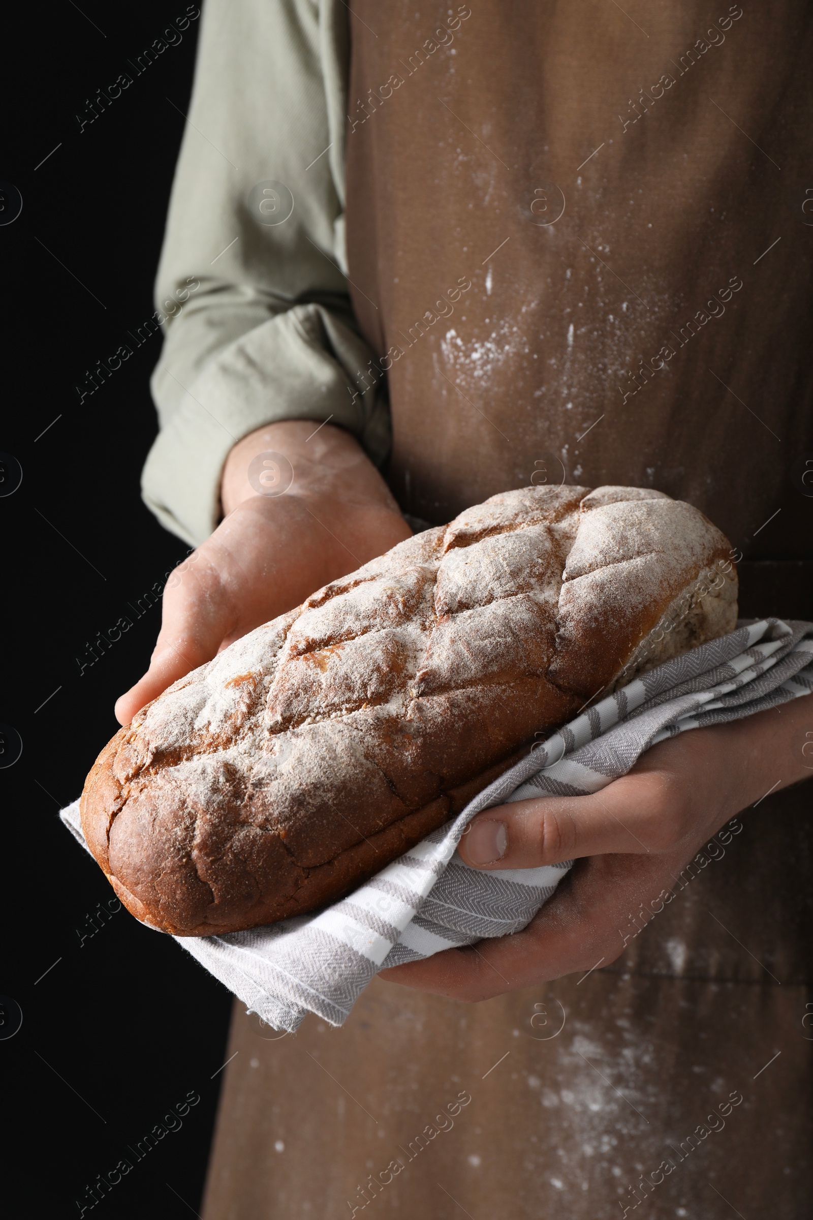 Photo of Woman holding freshly baked bread on black background, closeup