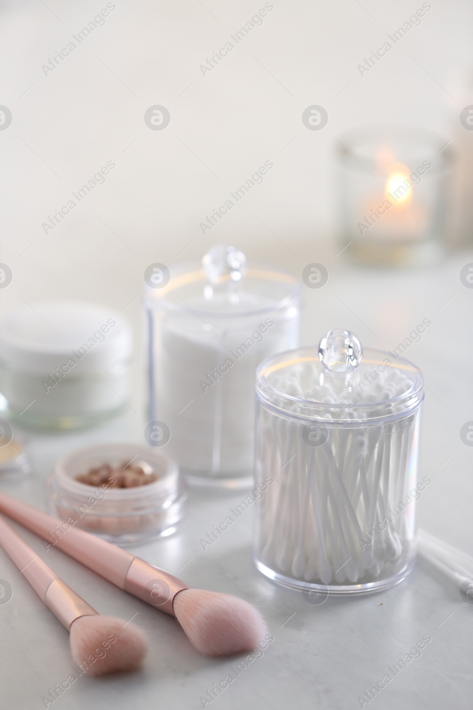 Photo of Cotton buds and pads in transparent holders near makeup brushes on table indoors