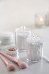 Cotton buds and pads in transparent holders near makeup brushes on table indoors