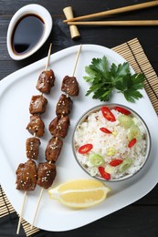 Photo of Tasty chicken meat glazed in soy sauce served with rice on black wooden table, flat lay