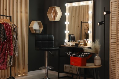 Makeup room. Stylish mirror near dressing table, chair and clothes rack indoors