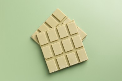 Photo of Pieces of tasty matcha chocolate bar on light green background, top view