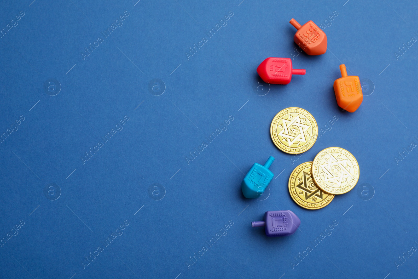 Photo of Dreidels with Jewish letters and coins on blue background, flat lay with space for text. Traditional Hanukkah game