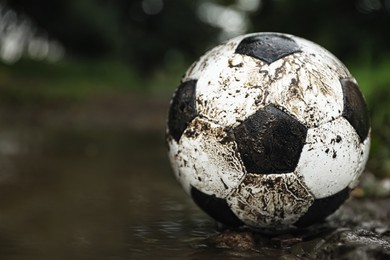 Dirty leather soccer ball in puddle outdoors, space for text