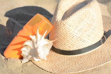 Stylish straw hat, sea shell and sunscreen on sandy beach, closeup