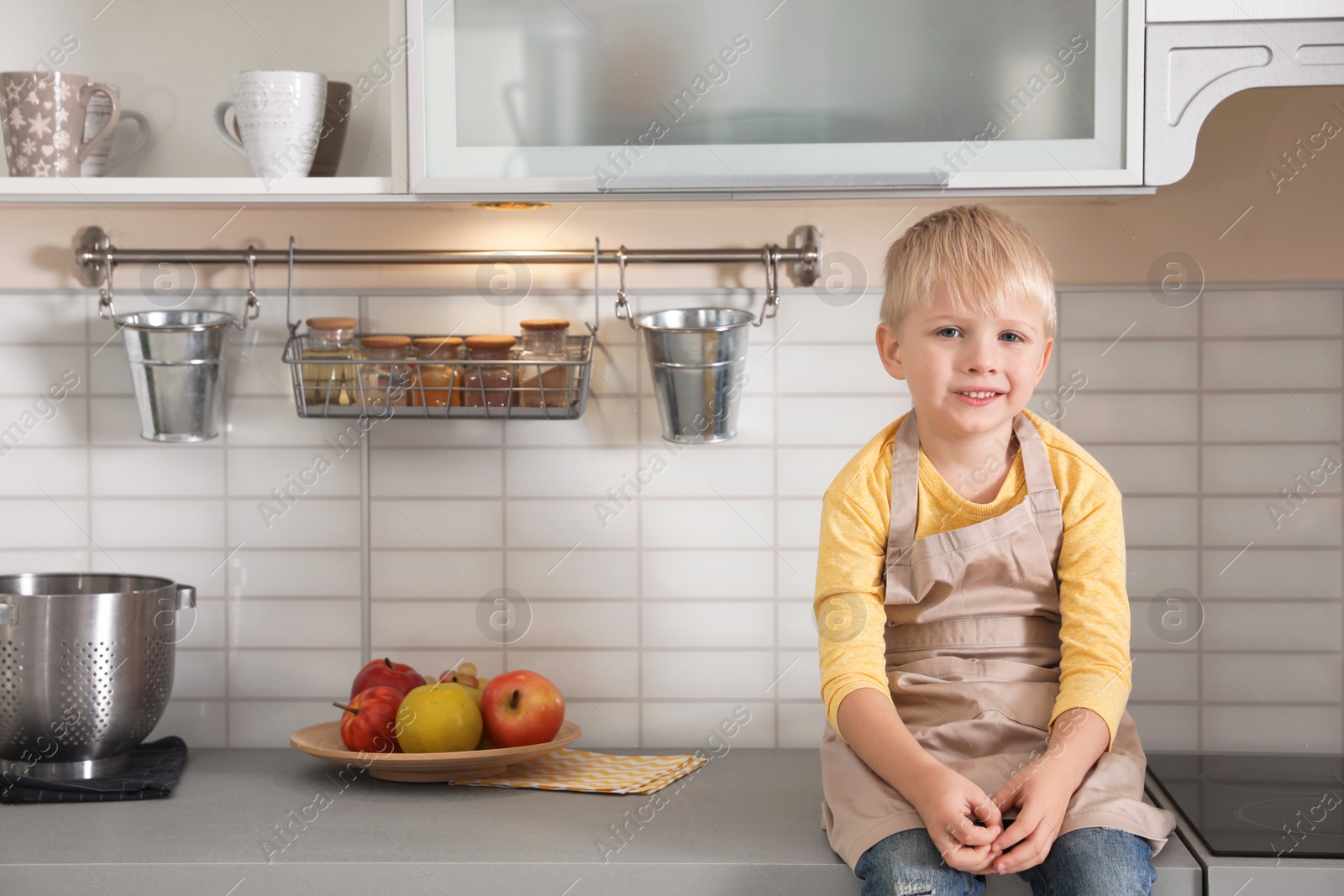 Photo of Cute little boy wearing apron in kitchen. Space for text