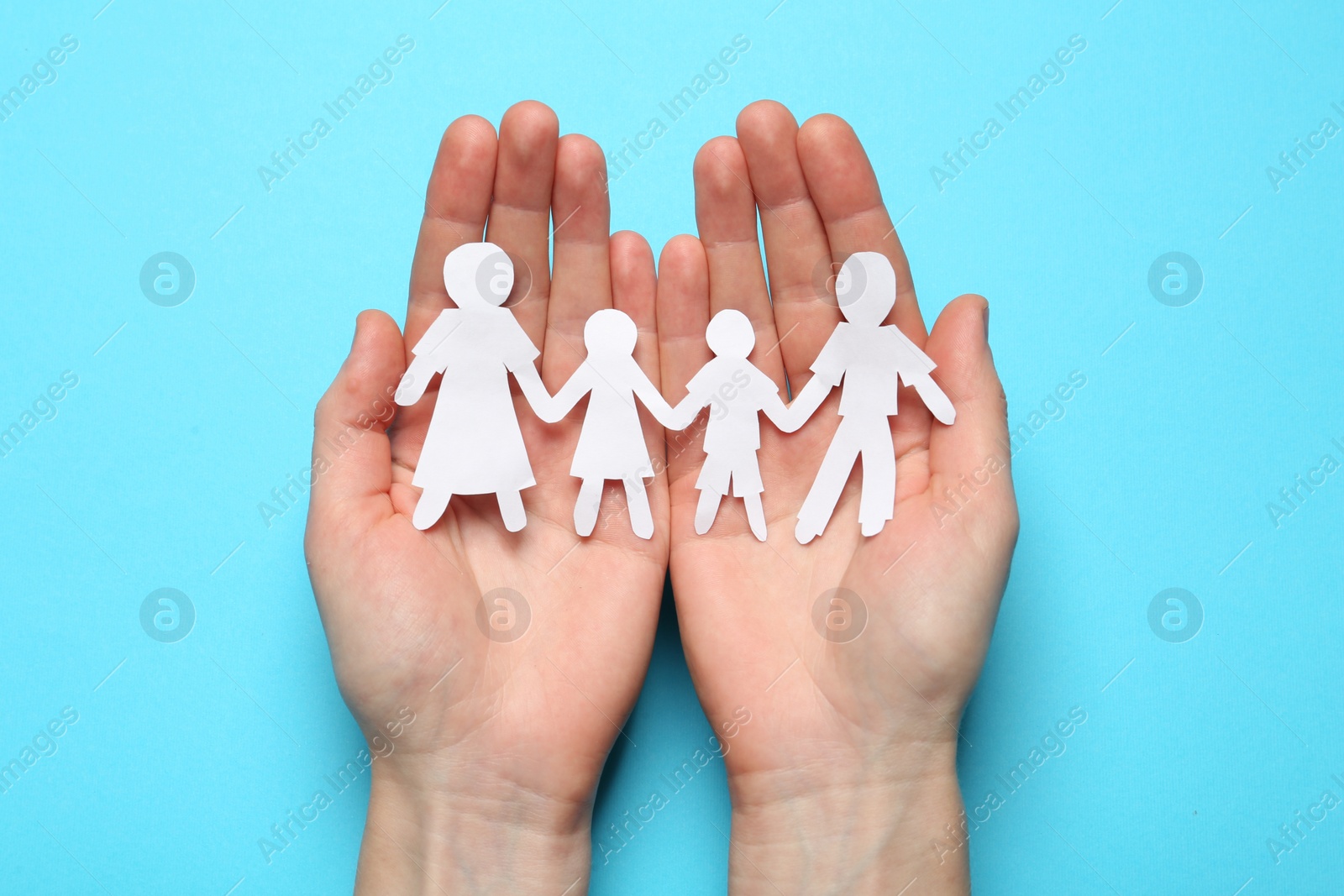 Photo of Woman holding paper cutout of family on light blue background, top view