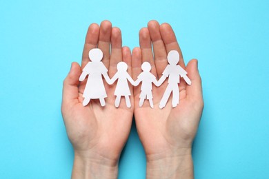 Woman holding paper cutout of family on light blue background, top view