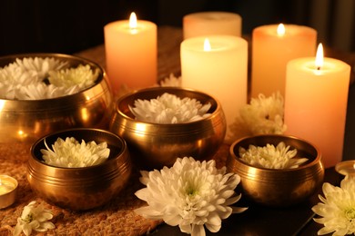 Photo of Tibetan singing bowls with water, beautiful flowers and burning candles on table