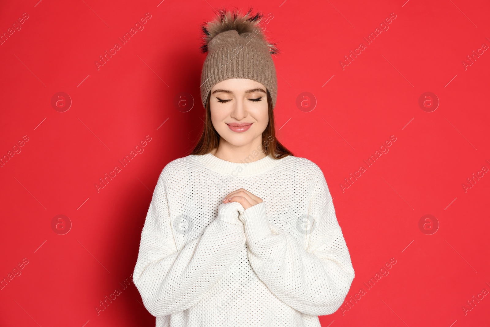 Photo of Young woman wearing warm sweater and hat on red background. Winter season