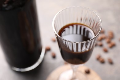 Photo of Bottle of coffee liqueur, shot glass and beans on light grey table, closeup