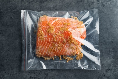 Photo of Raw salmon fillet with marinade in plastic bag on grey background, top view