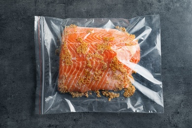 Raw salmon fillet with marinade in plastic bag on grey background, top view