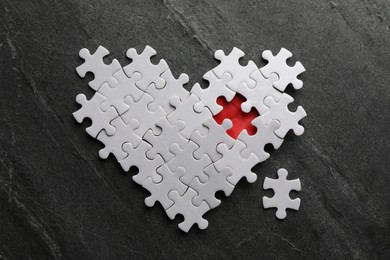 Heart made of puzzles with missing piece on black table