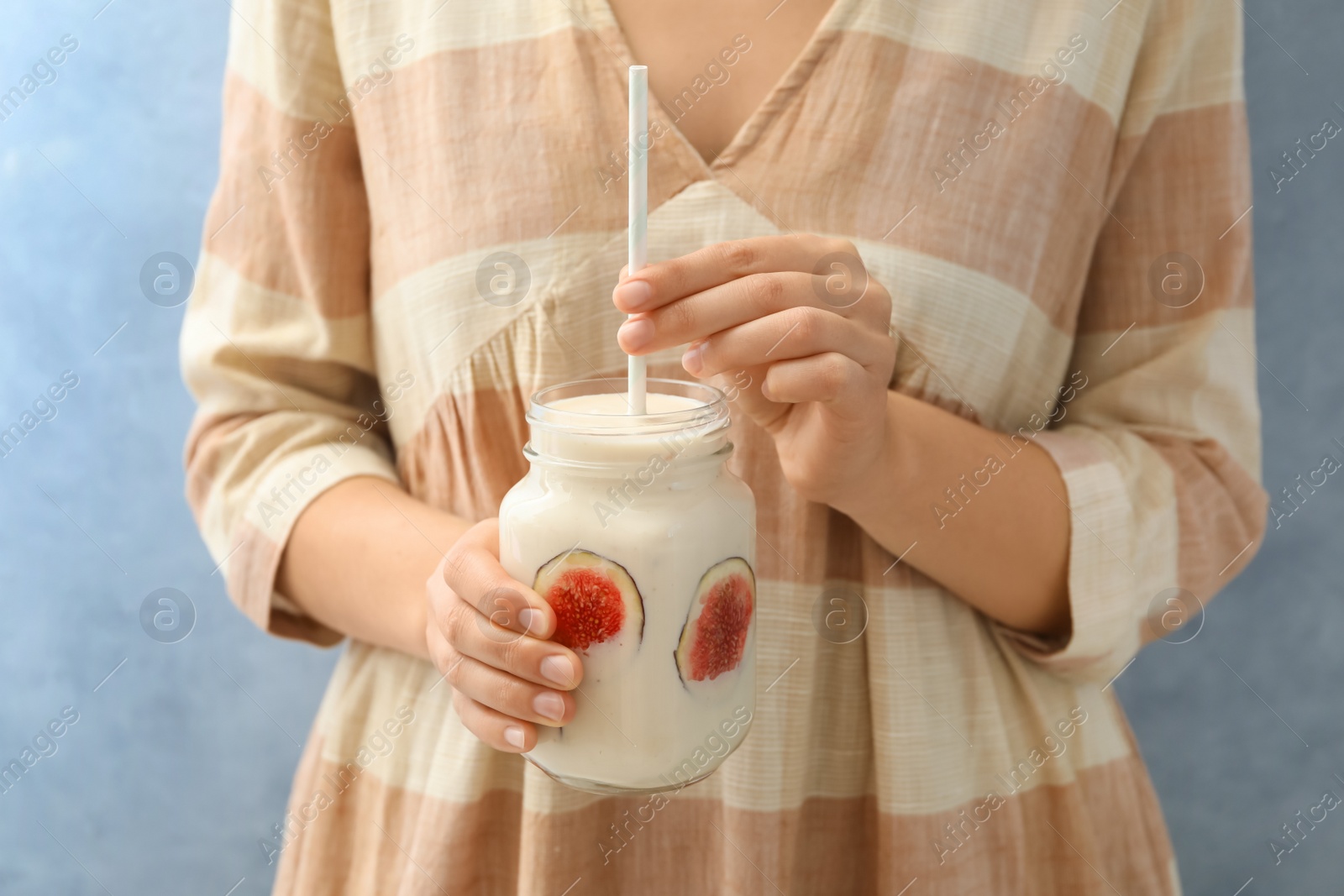 Photo of Woman holding mason jar with fig smoothie on light blue background, closeup