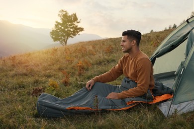 Photo of Man in sleeping bag near camping tent on hill