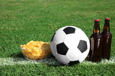 Photo of Soccer ball with beverage and chips on green football field grass