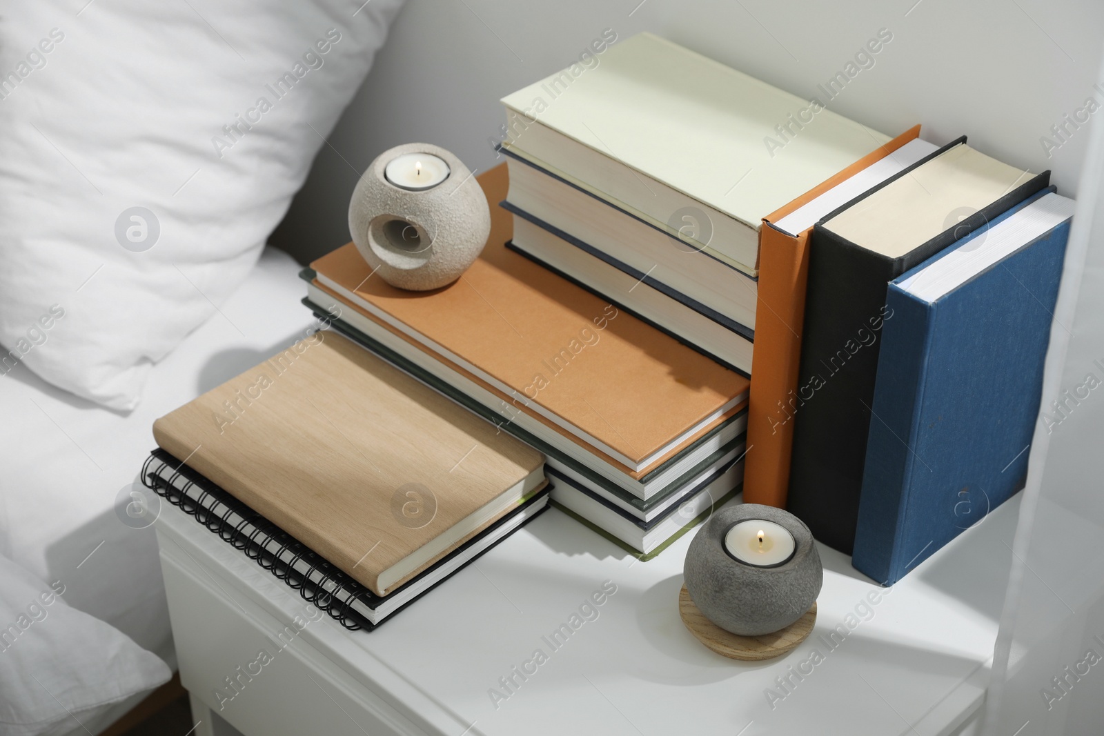 Photo of Hardcover books and scented candles on white bedside table indoors