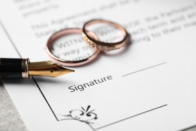 Photo of Marriage contract, fountain pen and wedding rings on table, closeup